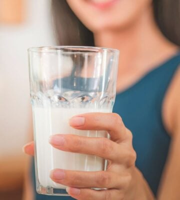 Photo shows a woman holding up a glass half full of milk