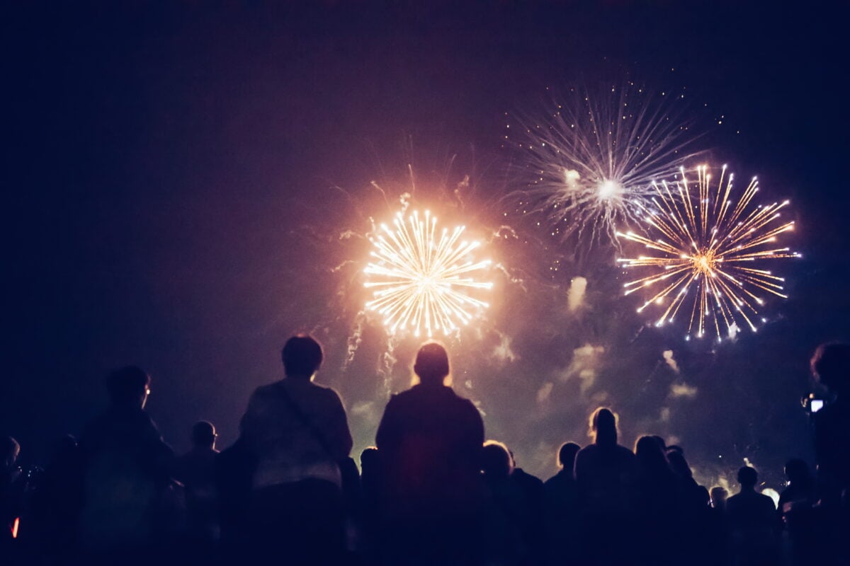 Photo shows the silhouette of a crowd from behind as they watch fireworks at night