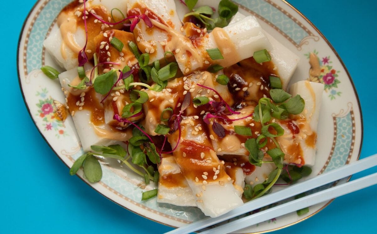 a picture of rice noodle rolls served with peanut and hoisin sauce and topped with spring onion