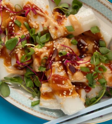 a picture of rice noodle rolls served with peanut and hoisin sauce and topped with spring onion