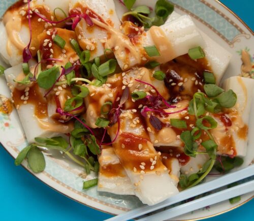 a picture of rice noodle rolls served with peanut and hoisin sauce and topped with spring onion