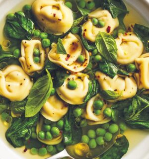 a bowl of bright vegan tortellini soup with lemon peel broth, peas, spinach, and chili