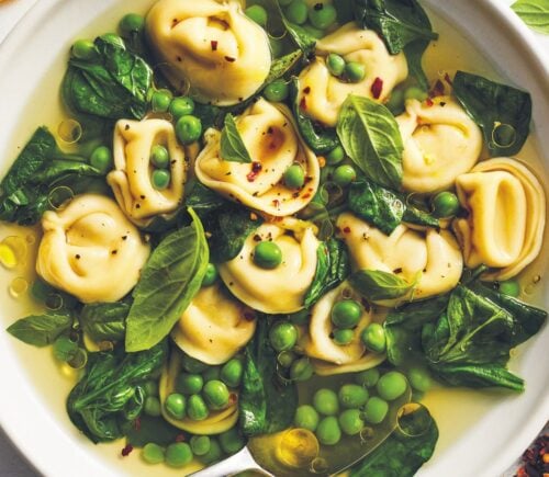 a bowl of bright vegan tortellini soup with lemon peel broth, peas, spinach, and chili