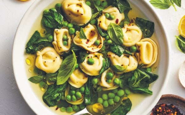 a bowl of bright vegan tortellini soup with lemon peel broth, peas, spinach, and chili