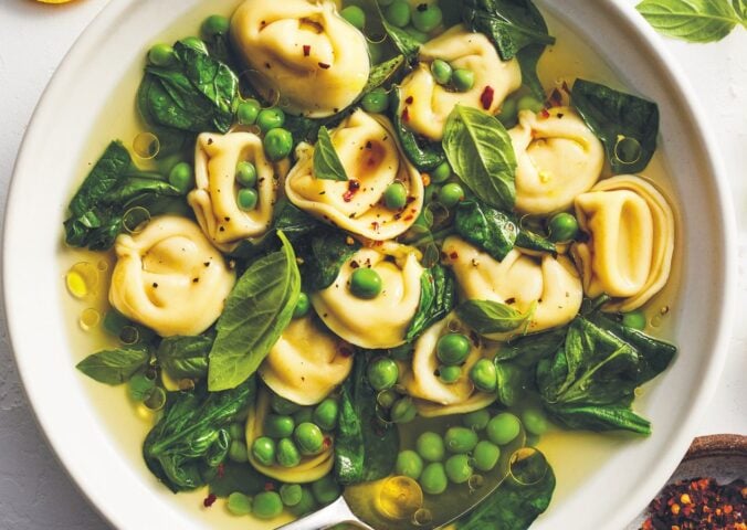 a bowl of bright vegan tortellini soup with lemon peel broth, peas, spinach, and chili