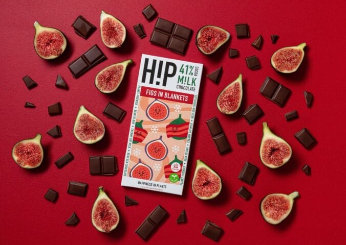 Photo shows the new H!P fig and vegan bacon chocolate bar on a red background, surrounding by pieces of chocolate, figs, and bacon