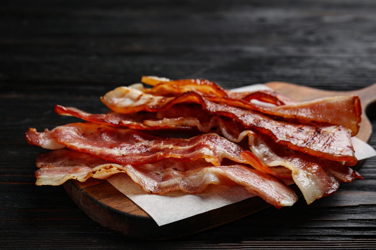 Photo shows crispy fried bacon slices on a wooden board on a table