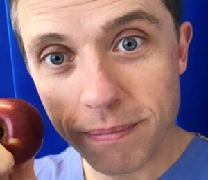 Renowned plant-based doctor Dr Alan Desmond holding an apple in front of some blue curtains at a hospital