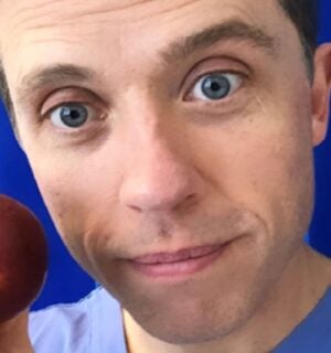 Renowned plant-based doctor Dr Alan Desmond holding an apple in front of some blue curtains at a hospital