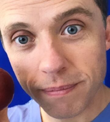 Renowned plant-based doctor Dr Alan Desmond holding an apple in front of some blue curtains at a hospital