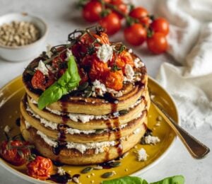 a stack of savory and vegan almond ricotta pancakes topped with cherry tomatoes and balsamic glaze