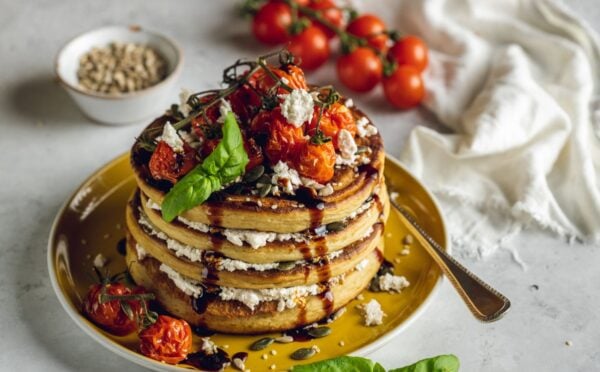 a stack of savory and vegan almond ricotta pancakes topped with cherry tomatoes and balsamic glaze