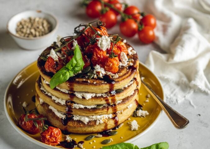 a stack of savory and vegan almond ricotta pancakes topped with cherry tomatoes and balsamic glaze