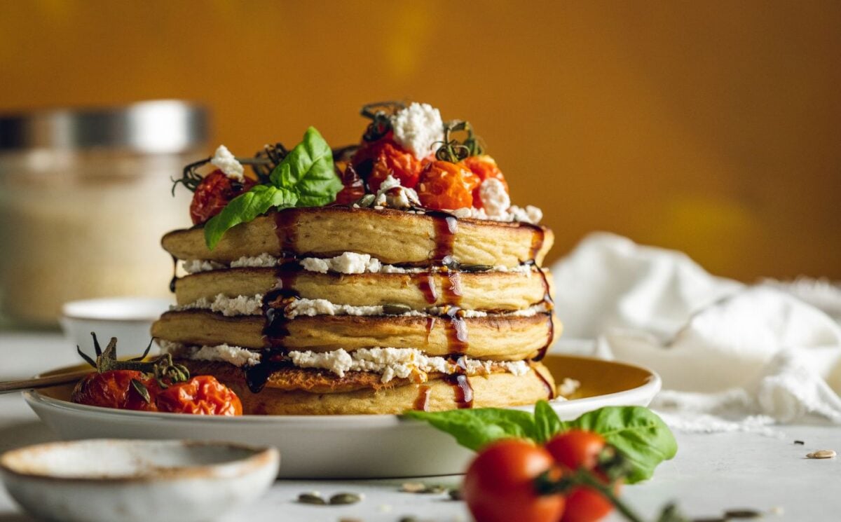 a stack of savory and vegan almond ricotta pancakes topped with cherry tomatoes and balsamic glaze