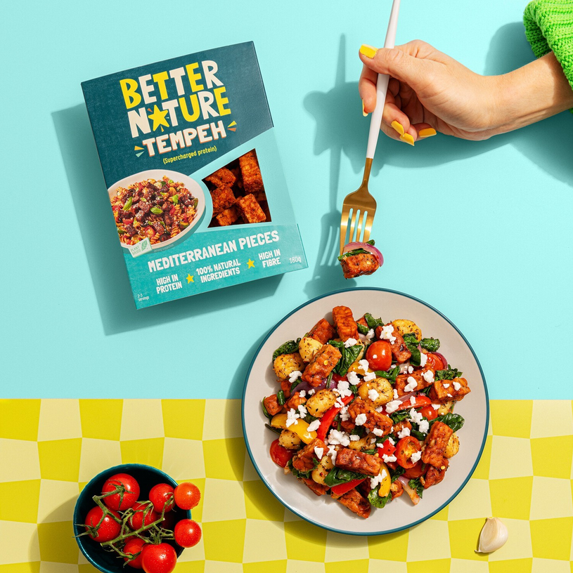 Photo shows a meal made with Better Nature tempeh, the product packaging, and a hand holding a fork against a blue and yellow background