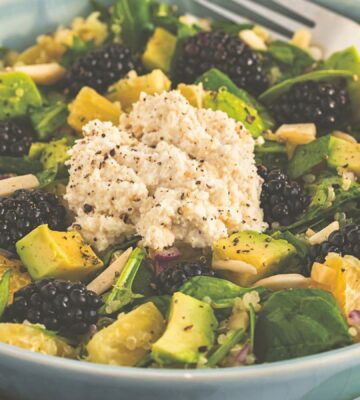 a bowl of bright and lively citrus salad made with quinoa, spinach, macadamia nut ricotta, and blackberries