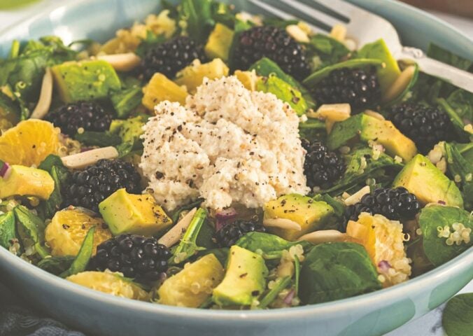 a bowl of bright and lively citrus salad made with quinoa, spinach, macadamia nut ricotta, and blackberries