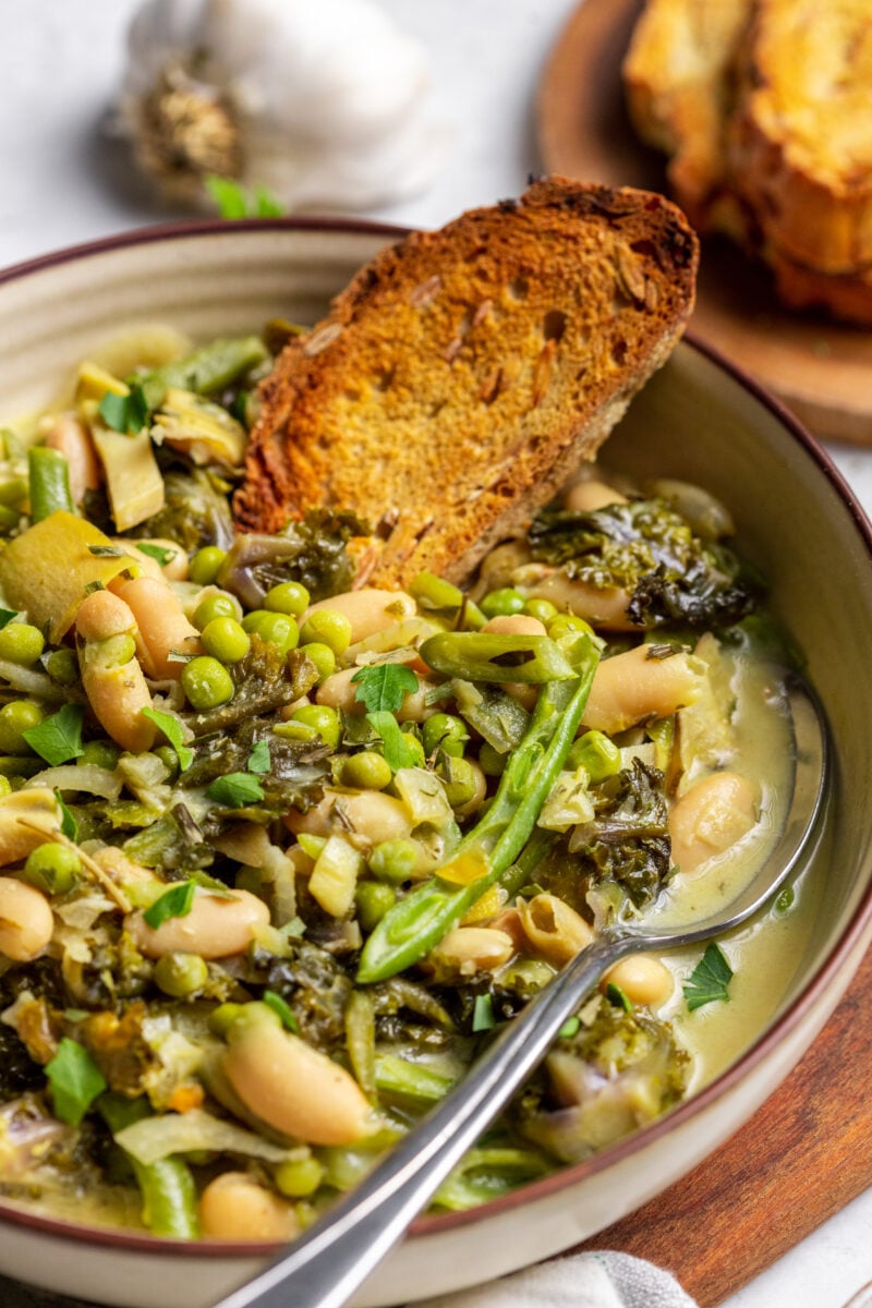 A bowl of green cannellini bean stew in a bowl with toasted bread