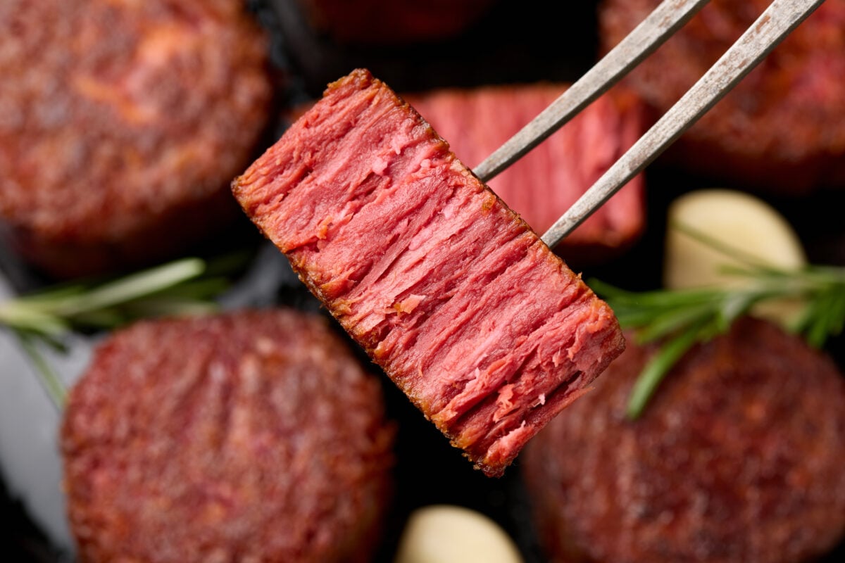 Photo shows a piece of plant-based steak held up to the camera on a fork so as to show the realistic grain of the meat