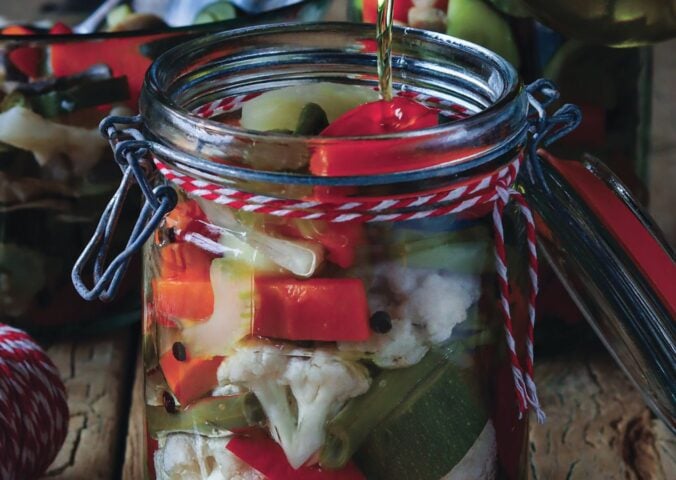 a jar of pickled vegetables with oil including cauliflower, capsicum, and carrots