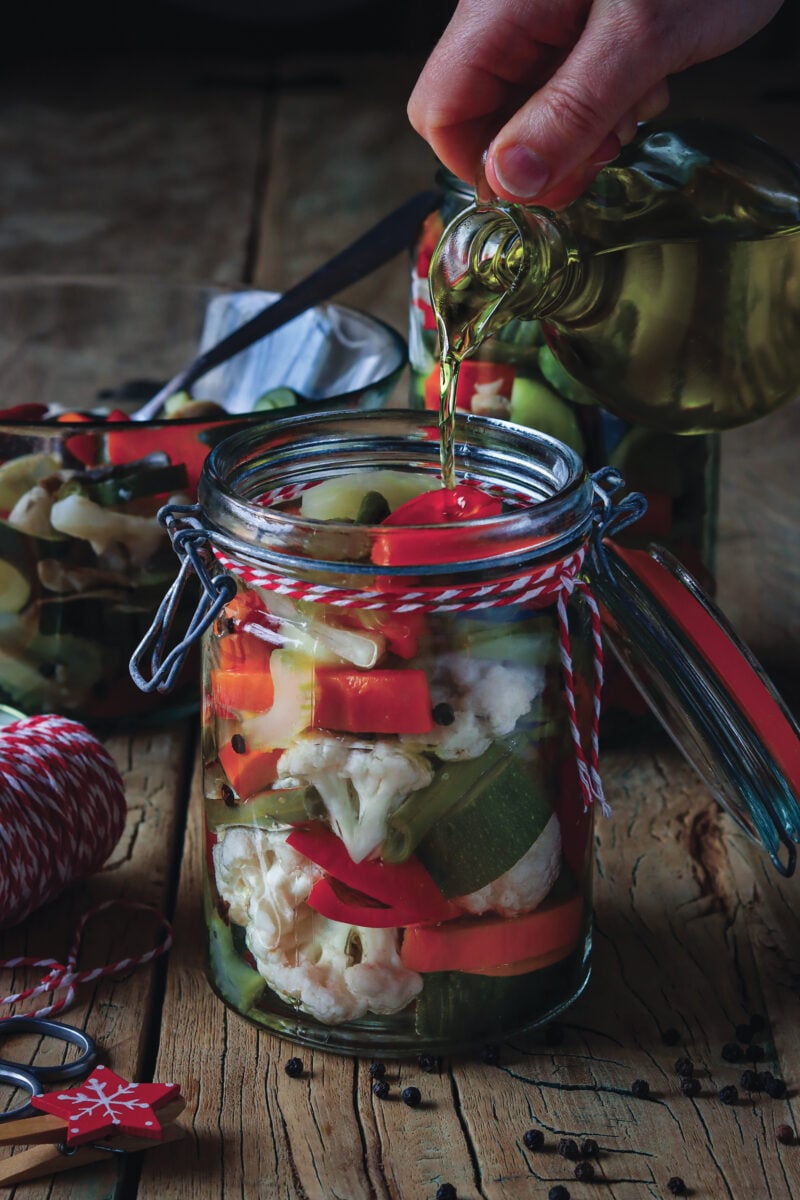 a jar of pickled vegetables with oil including cauliflower, capsicum, and carrots