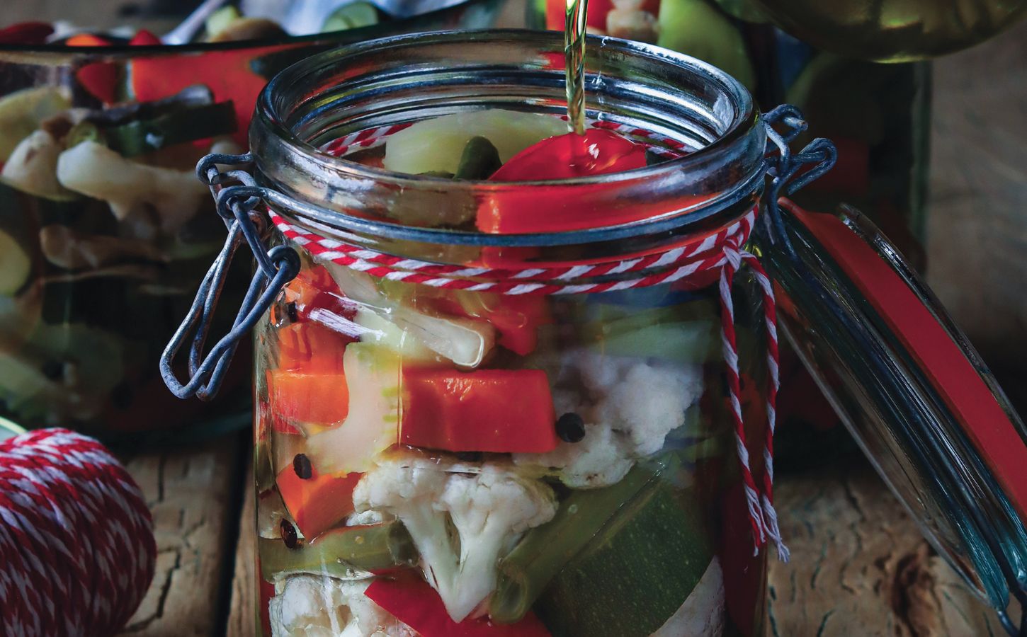 a jar of pickled vegetables with oil including cauliflower, capsicum, and carrots