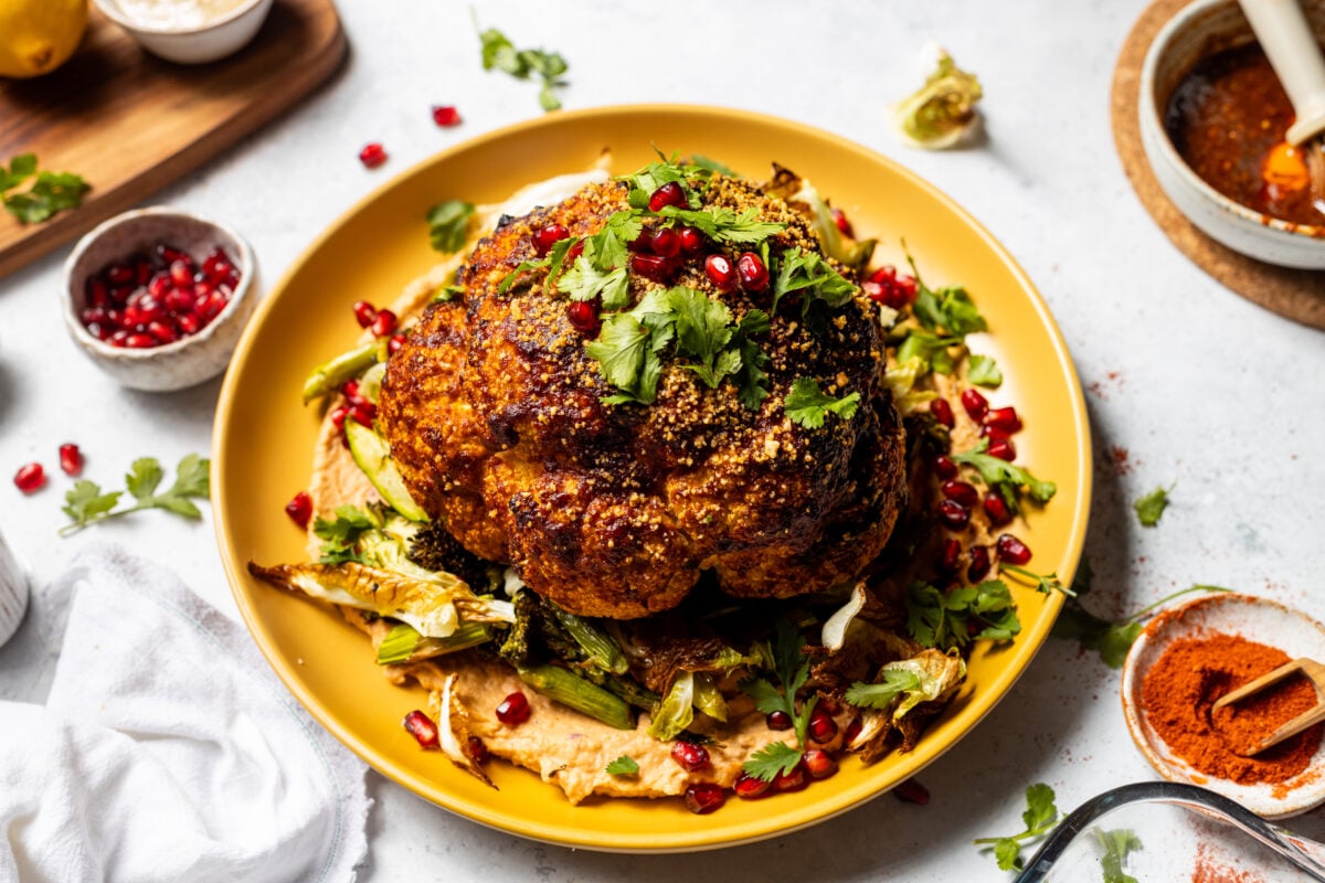 A vegan whole roasted cauliflower on a yellow plate