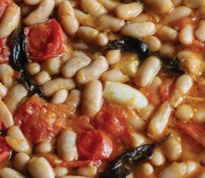 a close up of a vegan rustic tomato bean stew with sage and garlic