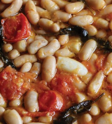 a close up of a vegan rustic tomato bean stew with sage and garlic