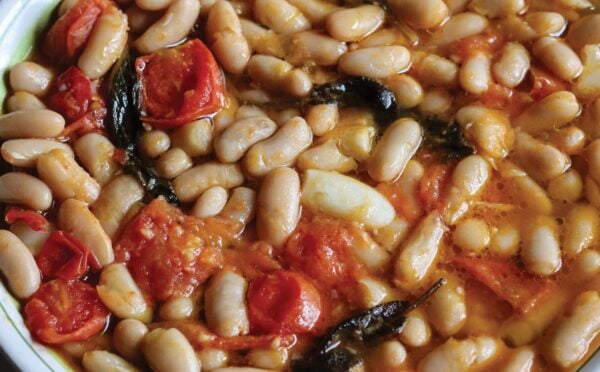 a close up of a vegan rustic tomato bean stew with sage and garlic