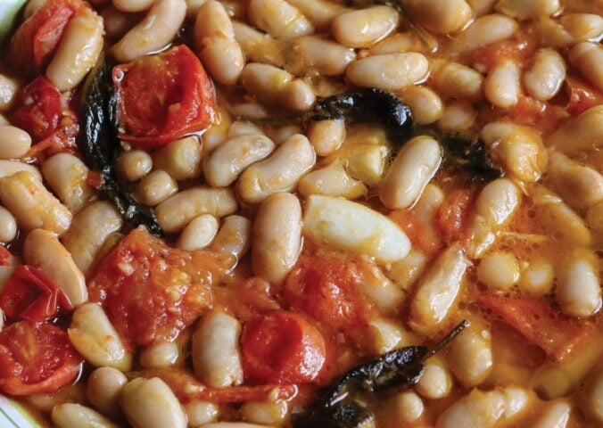 a close up of a vegan rustic tomato bean stew with sage and garlic