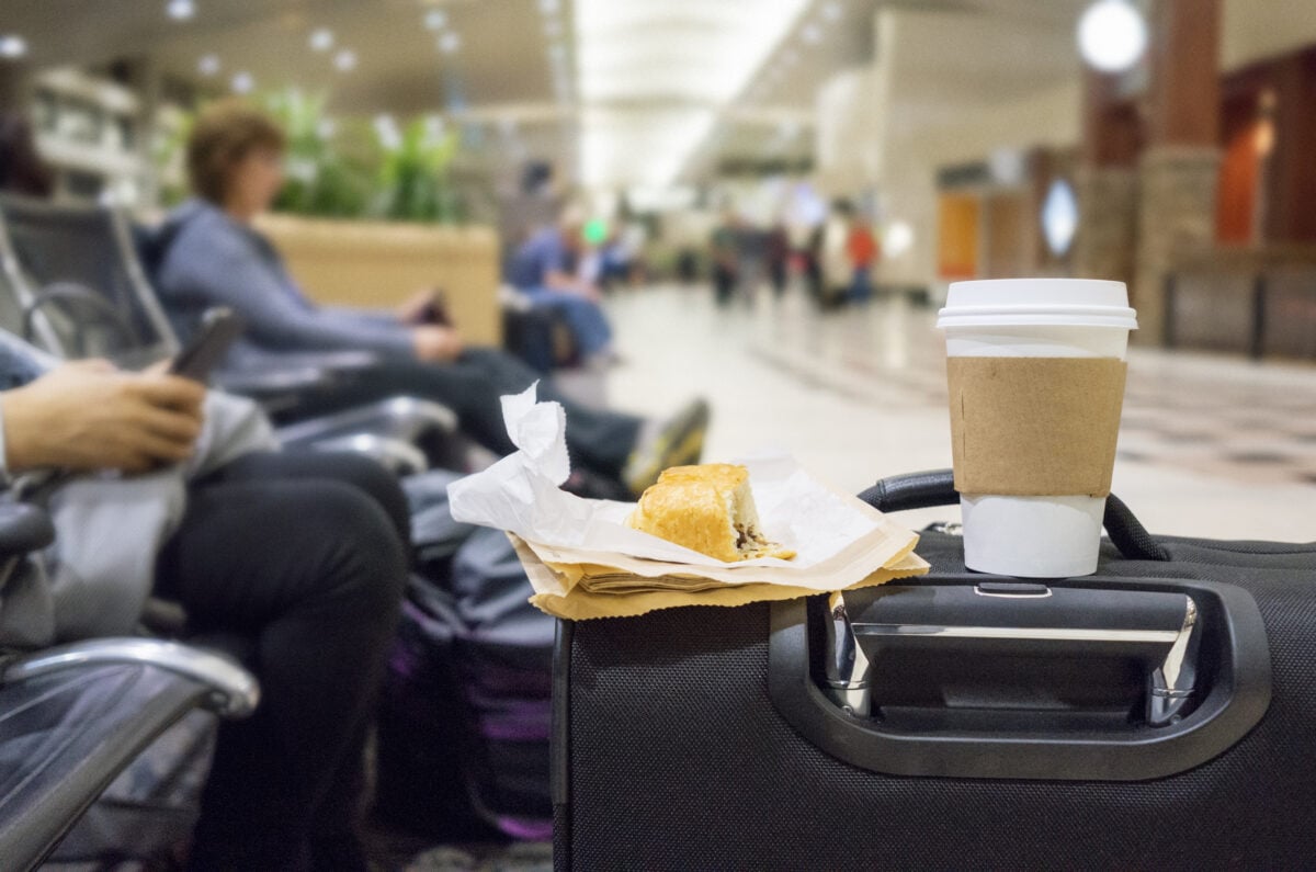 A pastry and coffee resting on a suitcase in an airport