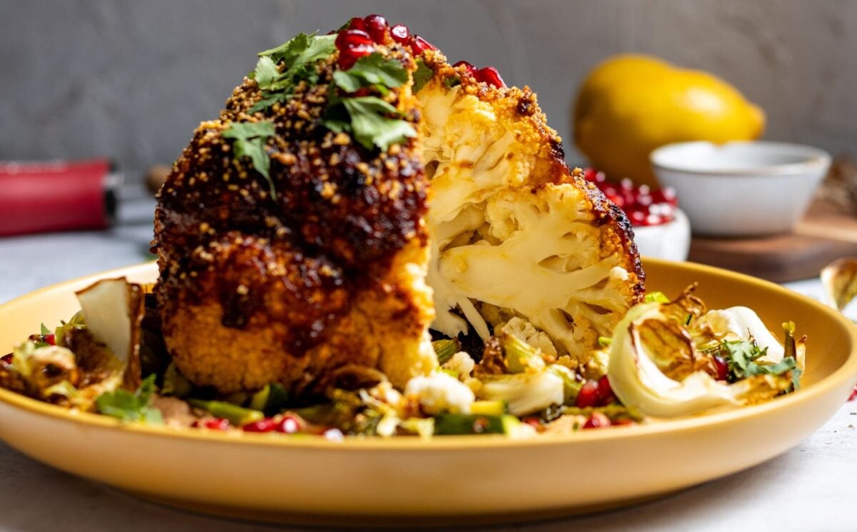 A vegan whole roasted cauliflower on a yellow plate