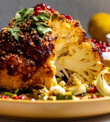 A vegan whole roasted cauliflower on a yellow plate