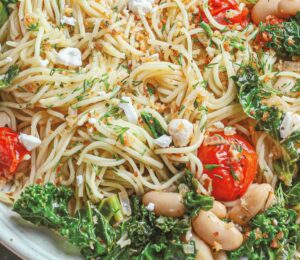 a bowl of angel hair with lemon kale and tomatoes with vegan feta