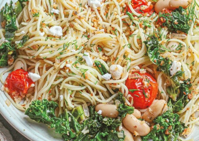 a bowl of angel hair with lemon kale and tomatoes with vegan feta