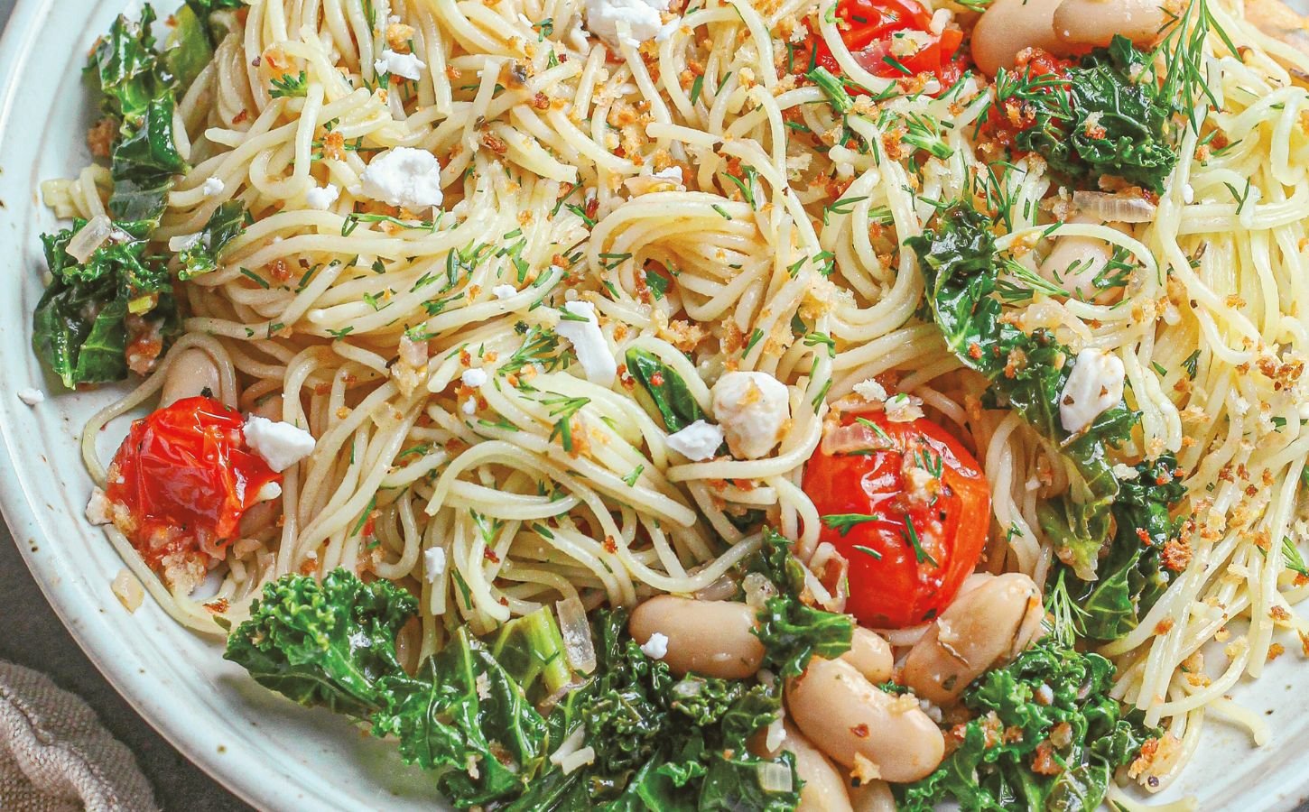 a bowl of angel hair with lemon kale and tomatoes with vegan feta