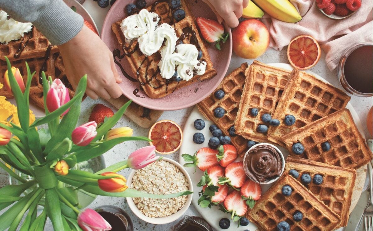 a spread of apple waffles served with fruit, vegan chocolate, and whipped cream