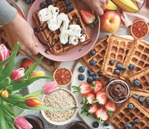 a spread of apple waffles served with fruit, vegan chocolate, and whipped cream