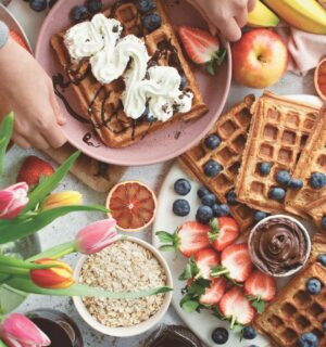 a spread of apple waffles served with fruit, vegan chocolate, and whipped cream