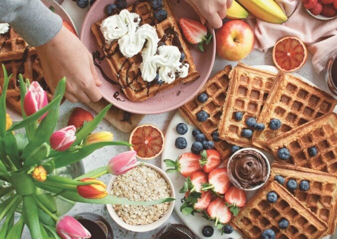 a spread of apple waffles served with fruit, vegan chocolate, and whipped cream