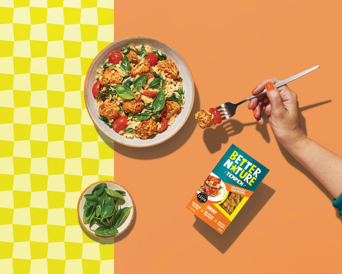 Photo shows Better Nature's tempeh as part of a meal and in its packaging against a peach and yellow background