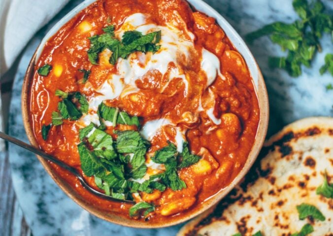 A bowl of vegan butter bean curry next to some naan