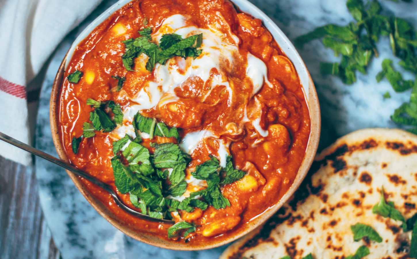 A bowl of vegan butter bean curry next to some naan