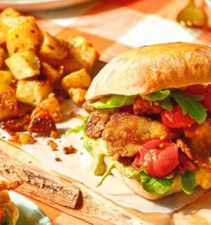 A crispy oyster mushroom vegan burger on a board next to some potatoes