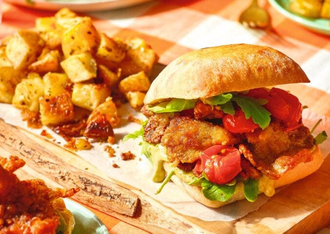 A crispy oyster mushroom vegan burger on a board next to some potatoes