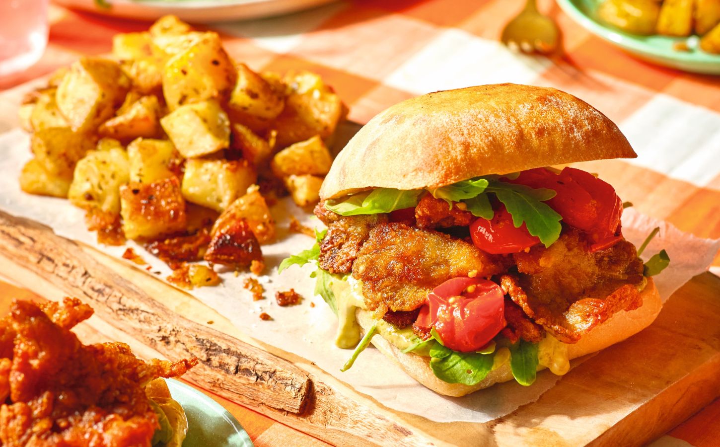 A crispy oyster mushroom vegan burger on a board next to some potatoes