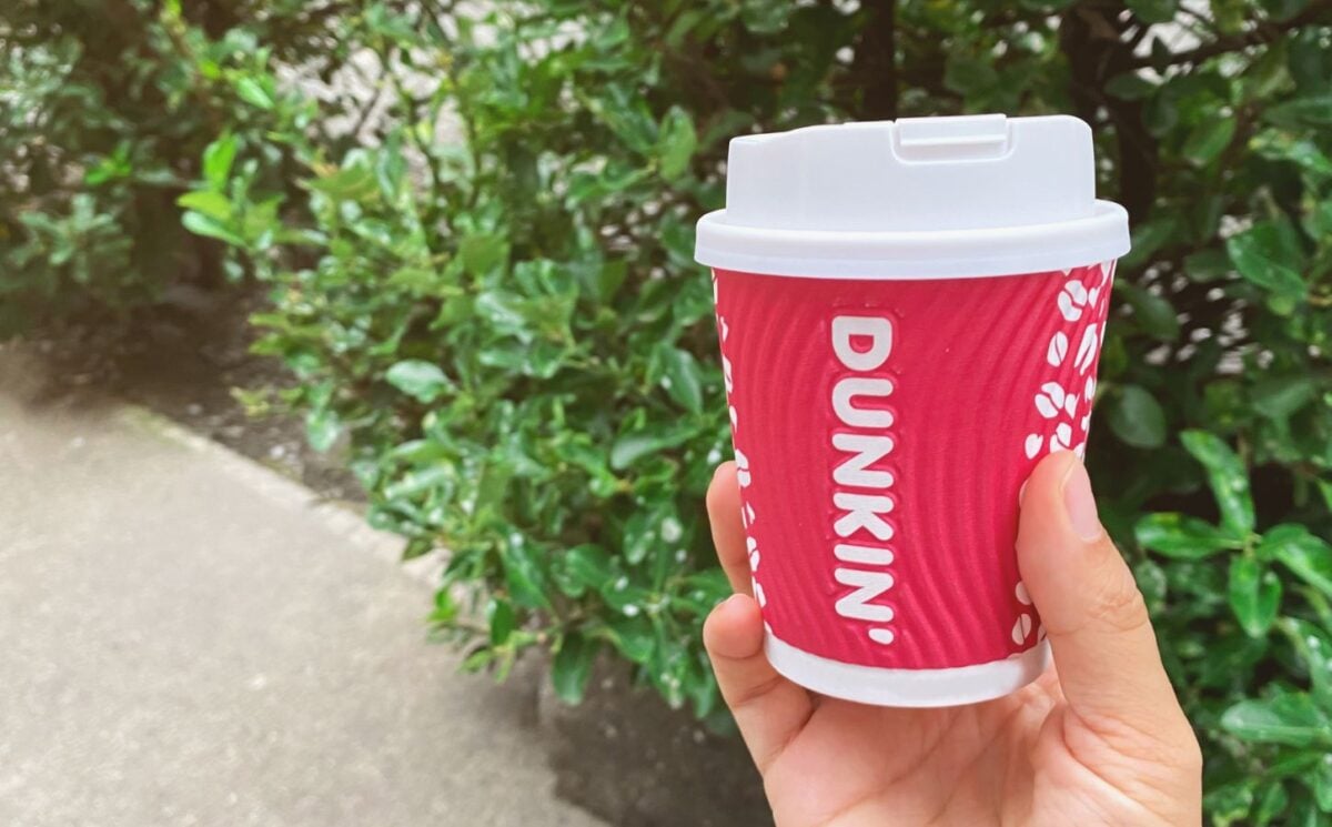 A person holding up a Dunkin' coffee cup