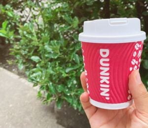 A person holding up a Dunkin' coffee cup