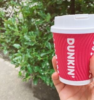 A person holding up a Dunkin' coffee cup